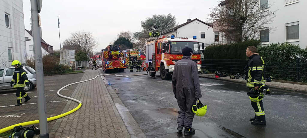 Einsatzkräfte der Feuerwehr bei den Nachlöscharbeiten an dem betroffenen Gewerbeobjekt. Der Einsatzbereich ist teilweise mit Löschschaum abgedeckt, Fahrzeuge und Geräte stehen rund um das Gebäude bereit.